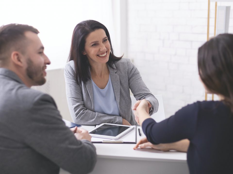 Positive insurance broker handshaking with young couple